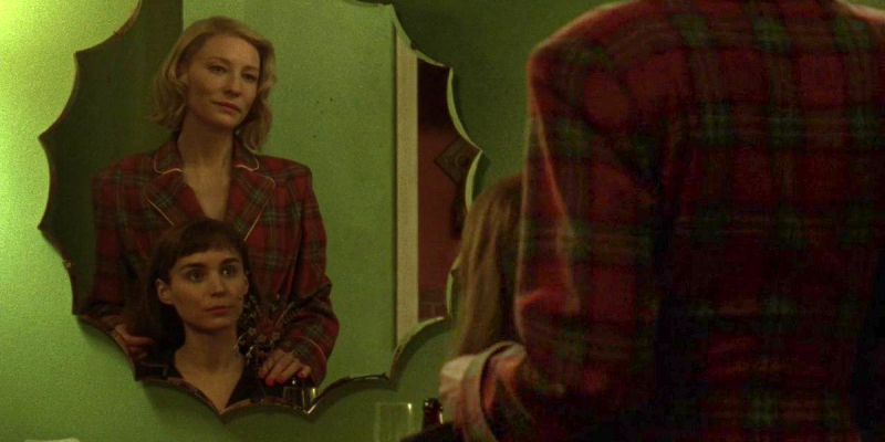 A still from Carol. Cate Blanchett stands behind Rooney Mara as they look at each other in a mirror. 
