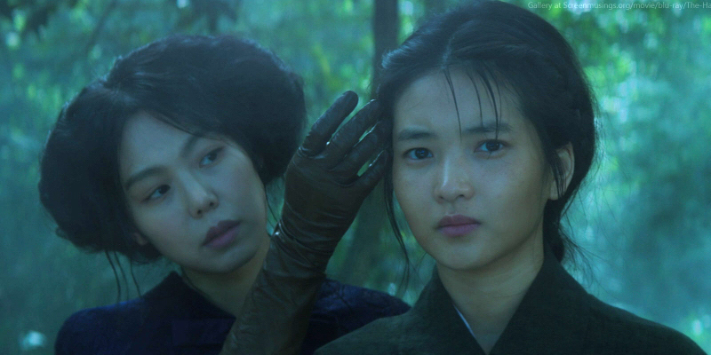 A still from the 11th best lesbian movie of all time The Handmaiden. A woman with a gloved hand brushes hair out of the face of another woman standing in front of her.