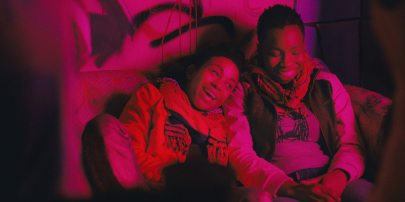 A still from the 3rd best lesbian movie of all time Pariah. Two girls laughing in a red-lit room.