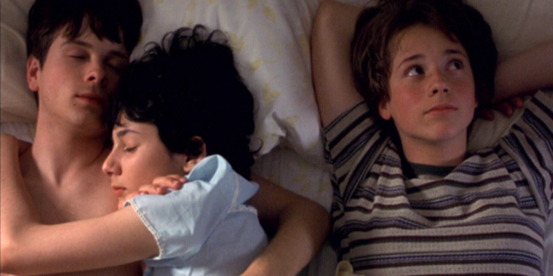 A still from Set Me Free. A girl with her eyes open lies in bed next to a boy and a girl cuddling while asleep.
