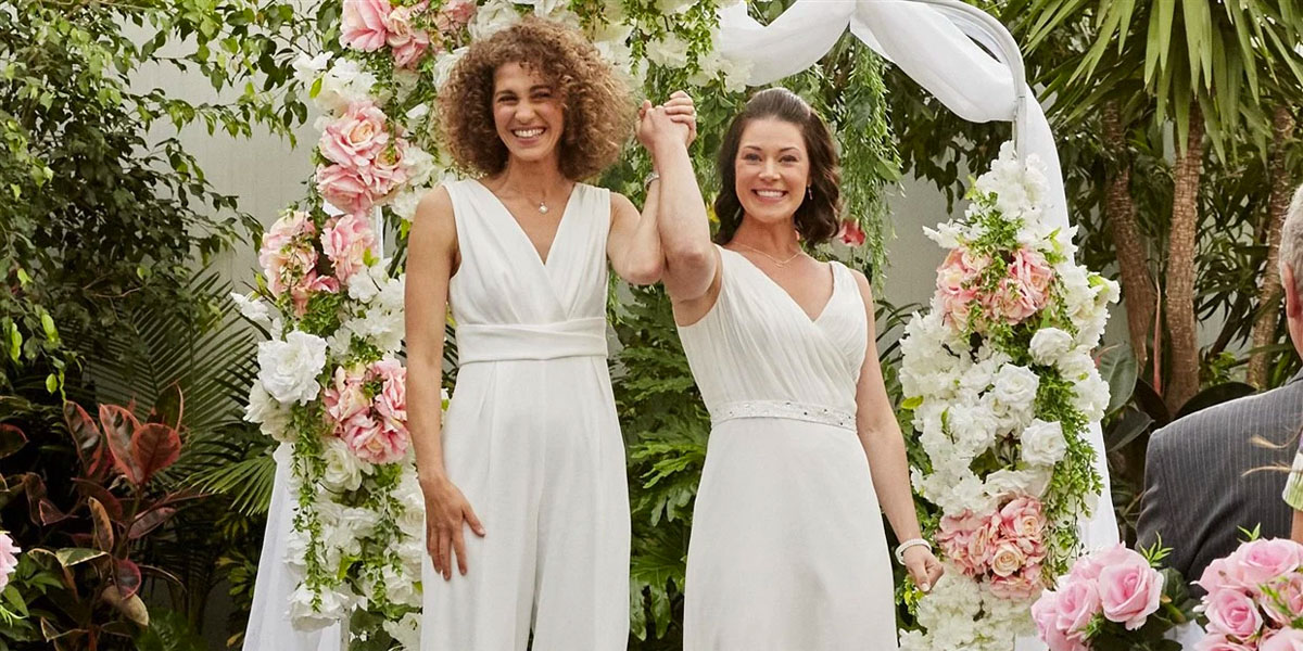Two lesbians in wedding gowns holding their hands triumphantly in the air in the new Hallmark movie Wedding Every Weekend.
