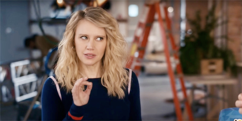 Kate McKinnon is in a navy blue sweatshirt with her hair down, she's making the OK symbol with her right hand and stares off to the side to make her point.