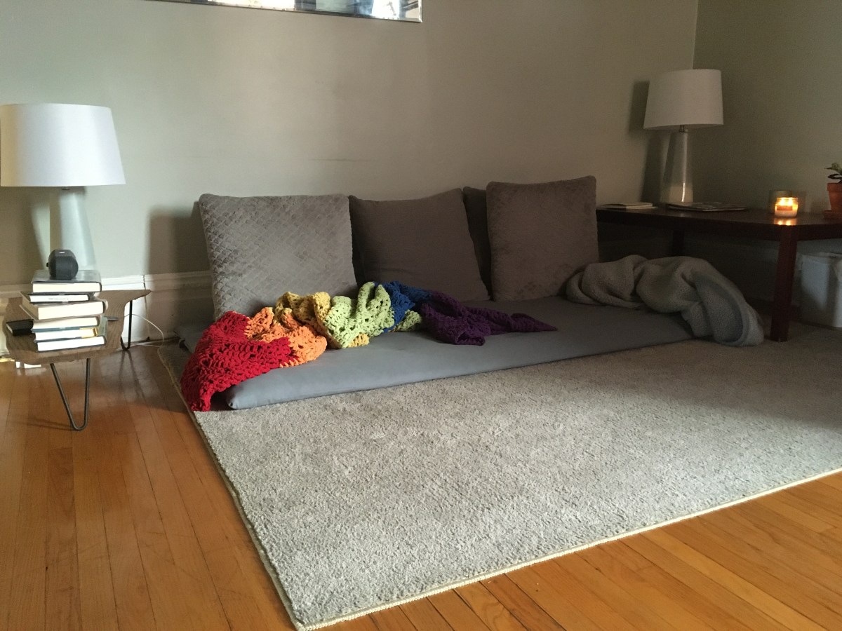 Grey couch sitting on the the floor, on top of a beige rug sitting on medium-toned hardwood