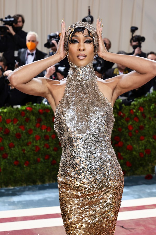 Mj Rodriguez in head to toe silvery sleeveless gown with a high neckline, her hands are on her head showing off her silver cap