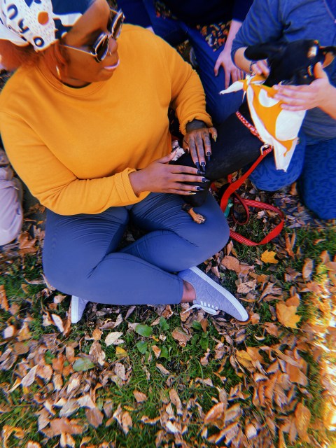 Shelli sitting in the grass with one of the dogs after the walk, they are matching in a mustard yellow bandanas.