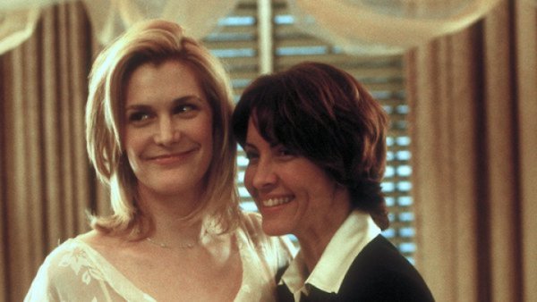 two lesbians getting married, one with dark short hair in a suit and the other in a white dress with blonde hair