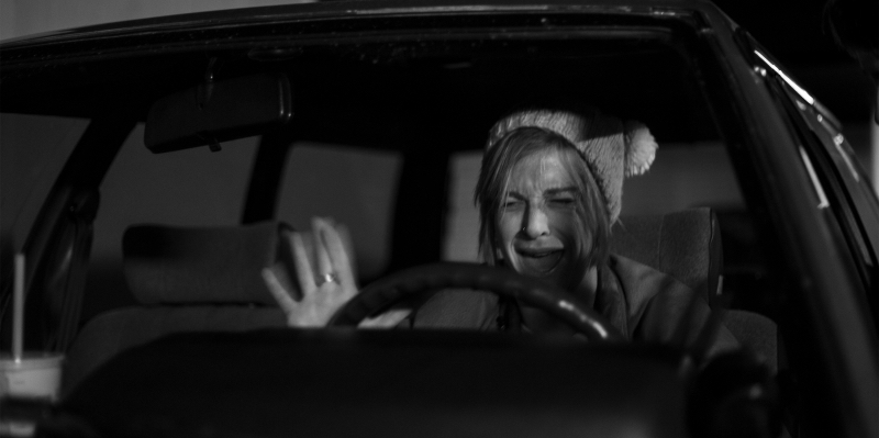 A black and white image of a woman freaking out in a car.