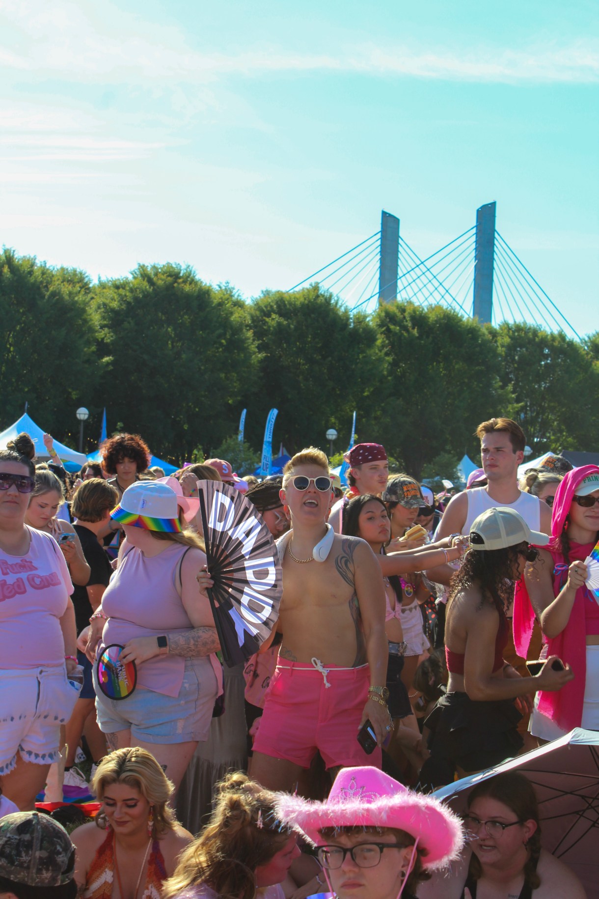 The crowd at Kentuckiana Pride, including someone with top surgery scars holding a DADDY fan