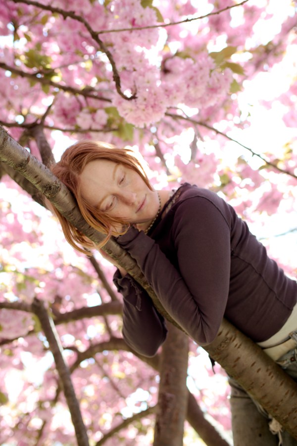 Bobbi lies in a tree with pink flowers blooming around them