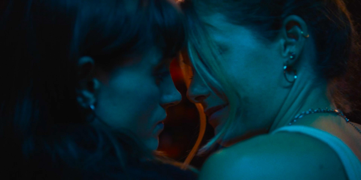 Chestnut: Natalia Dyer and Rachel Keller lean their heads together and almost kiss in blue club light