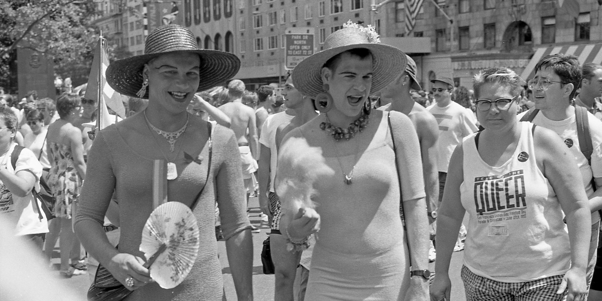 Two trans women smile at the 25th anniversary march of Stonewall next to a person in a tank that says Year of the Queer