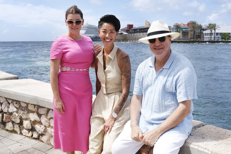 Pictured: (l-r) Gail Simmons in a pink dress, Kristen Kish in khaki sleeveless separates, Tom Colicchio in a hat, shades and linen.