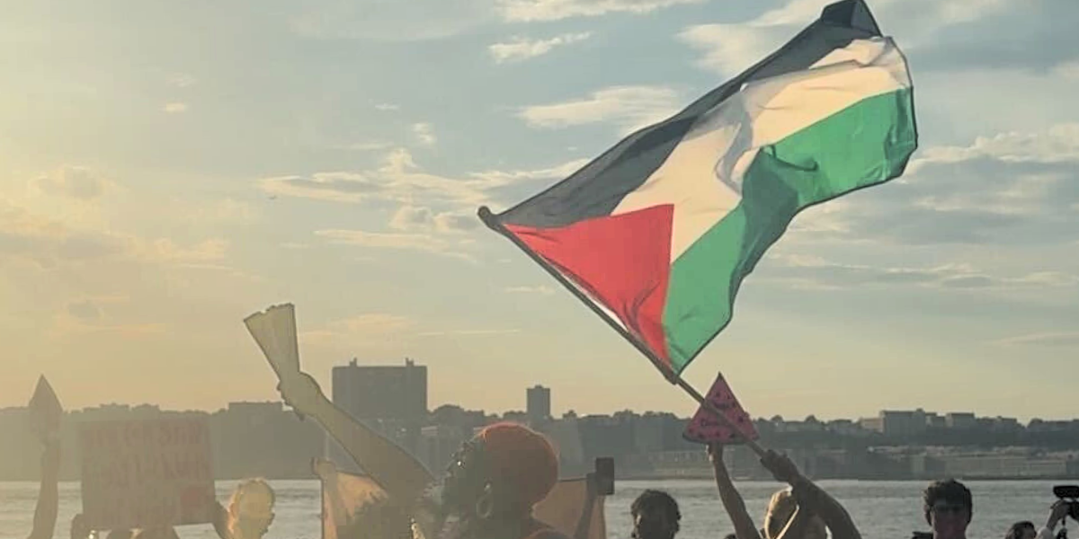 ACT UP NY's action against Outright International. A Palestinian flag waves in the Sunset as an activist lifts a fan in the air.