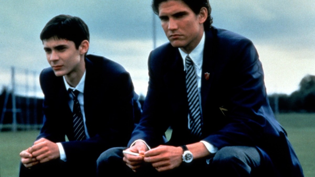 Two boys in school uniforms sit next to each other on a field.