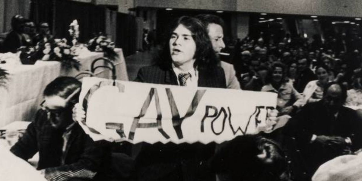 a historical image of a person holding a sign that reads GAY POWER