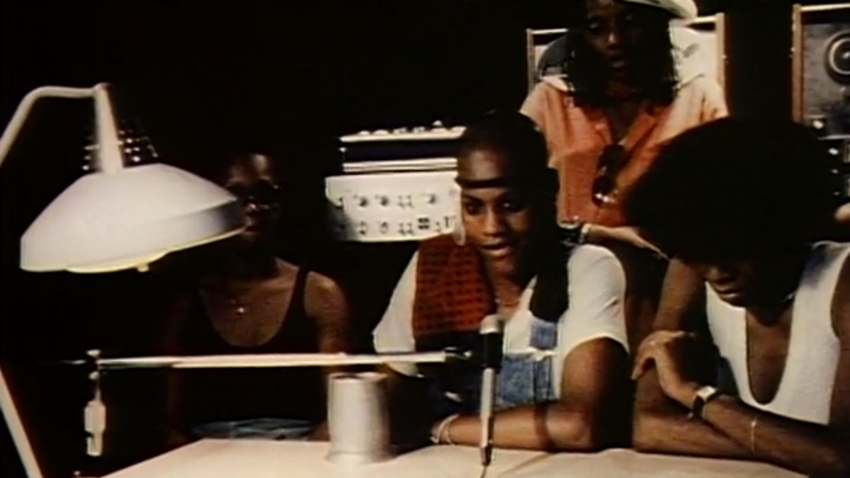 A group of Black women sit behind a microphone.