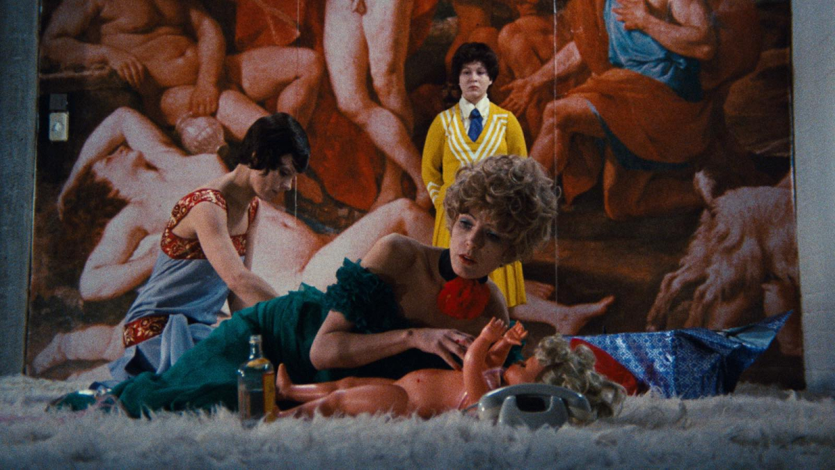 Best lesbian movies #30: a woman holds a baby doll by a phone while two other women are behind her and a mural behind them.