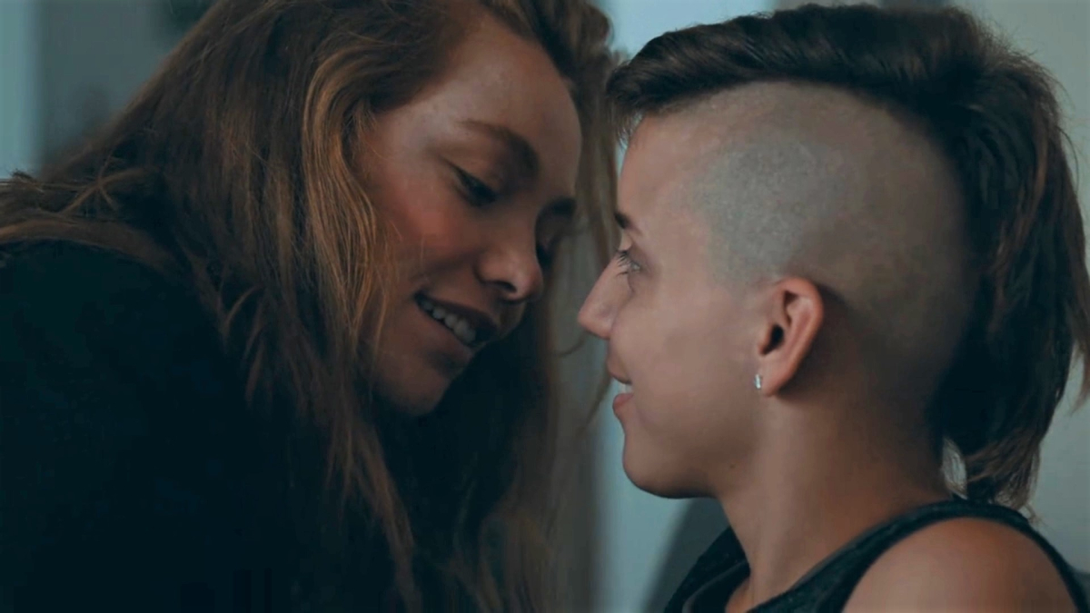 A femme with long hair leans in to kiss a nonbinary person with a mohawk and shaved head.