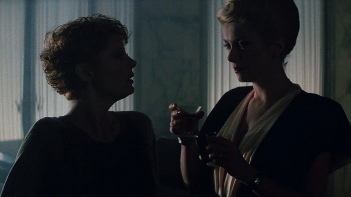 Catherine Deneuve gives Susan Sarandon a drink cloaked in shadow.
