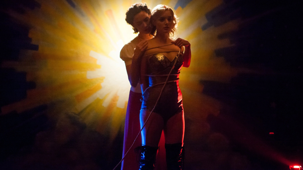 A woman embraces another woman dressed in Wonder Woman garb with a glowing gold light behind them.