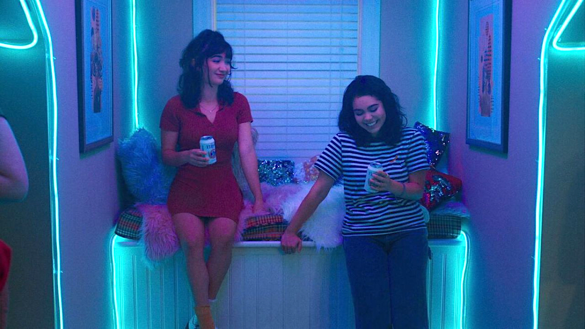 Rowan Blanchard and Auli'i Cravalho talk at a party in turquoise light 