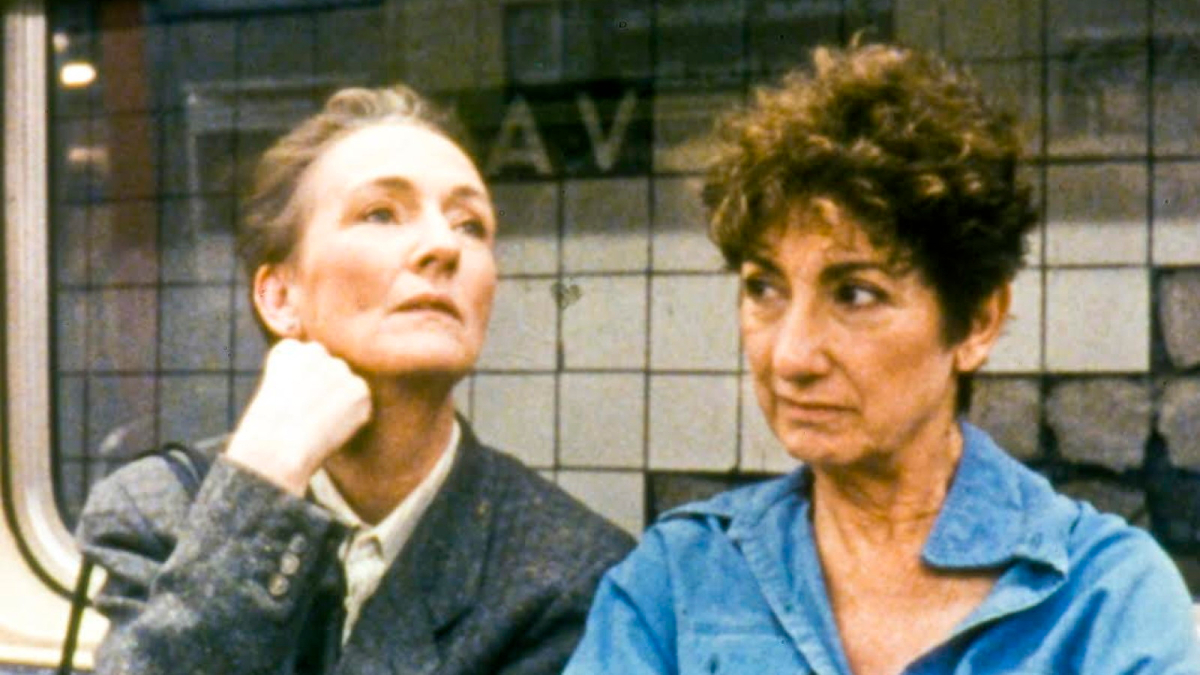 Two older women with short hair sit next to each other on the subway.