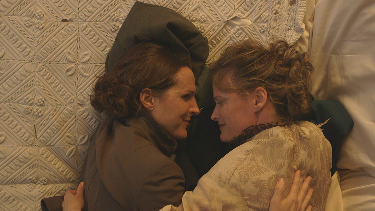 Best lesbian movies #80: two women lie in bed in period dress and make eye contact