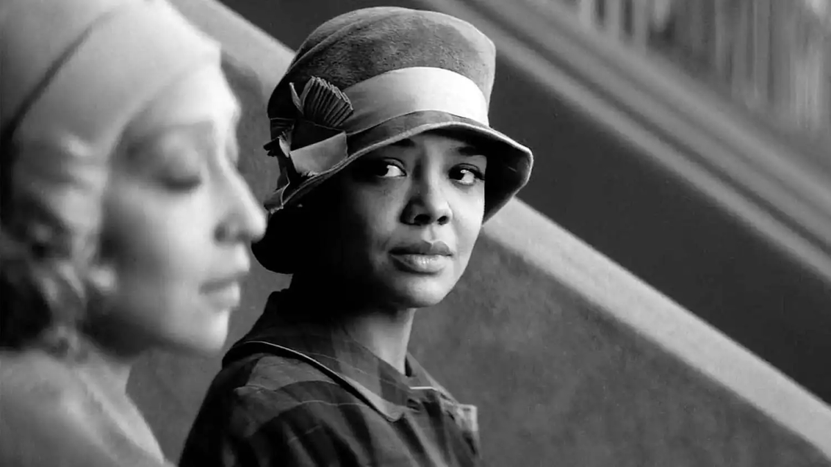A black and white image of Tessa Thompson looking at Ruth Negga in period dress.