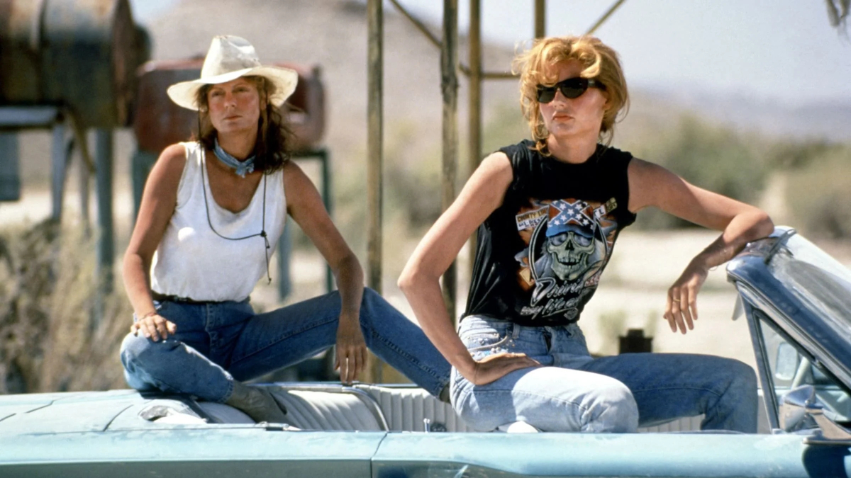 Geena Davis and Susan Sarandon sit on the edge of a convertible.
