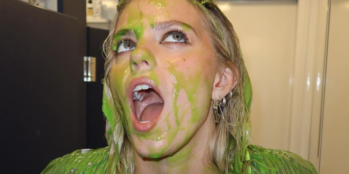A close up on Renee Rapp with her mouth open and slime on her face