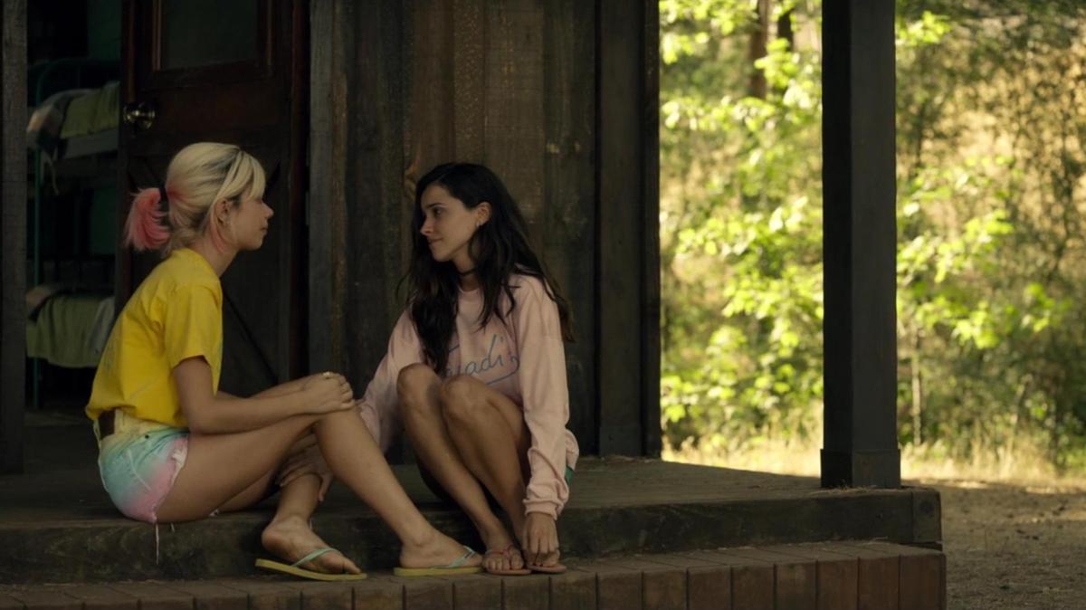 Two teen girls sit on the steps of a summer camp cabin