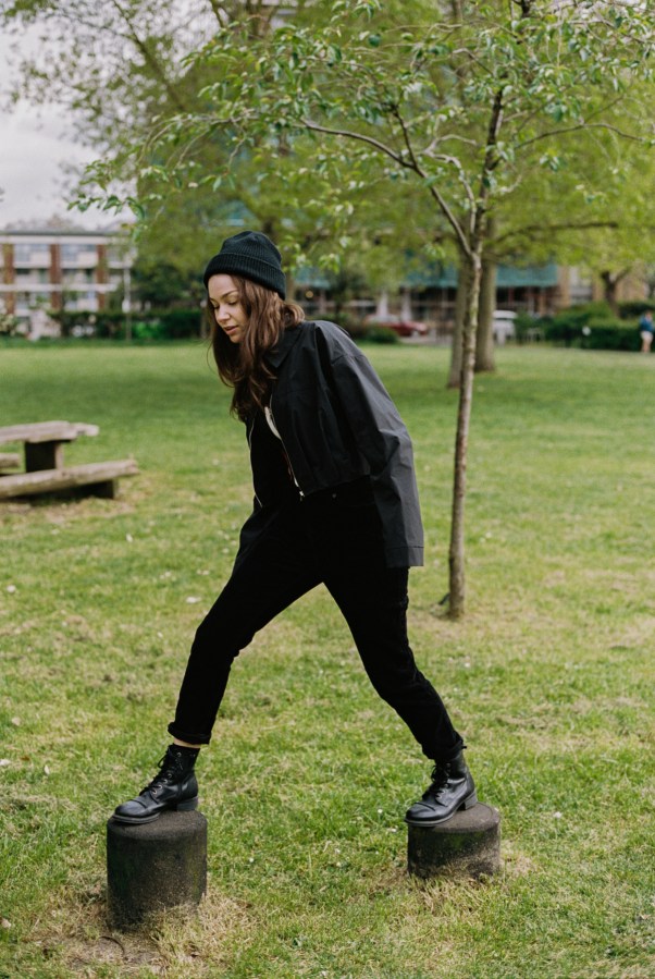 Minke dressed in black walks on stone stumps in a park.