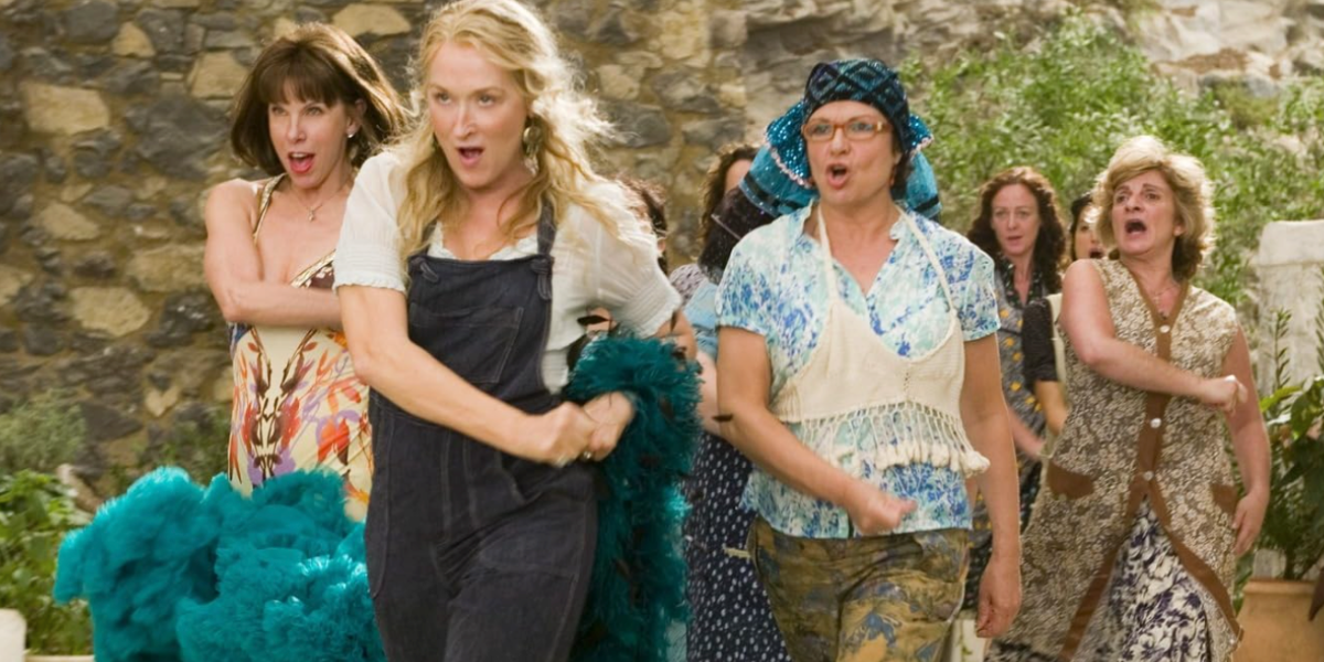 Meryl Streep in overalls sings as other Mamma Mia cast members follow behind herr