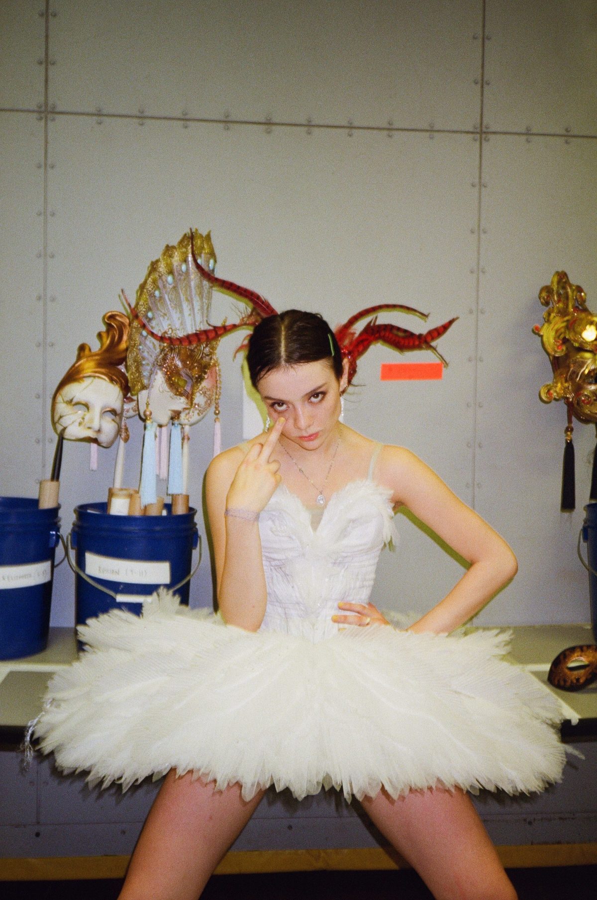 Shaelynn Estrada leans against a costume table in a white tutu with a middle finger up