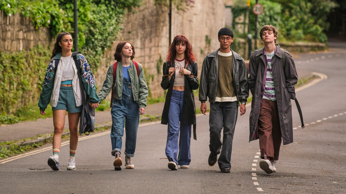 The teens of A Good Girl's Guide to Murder walk down the street, Pippa and Cara holding hands