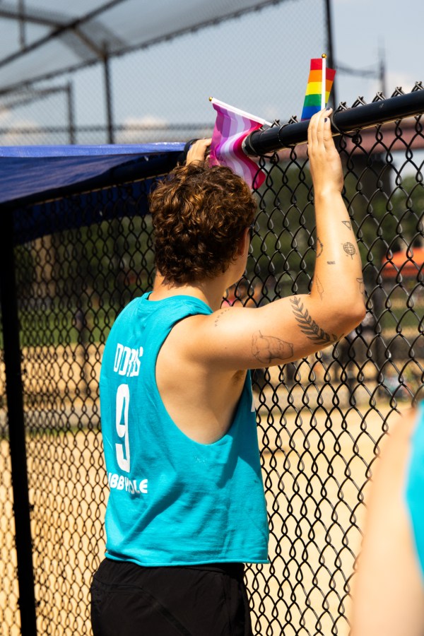 a softball player stands at a fence next to pride flags