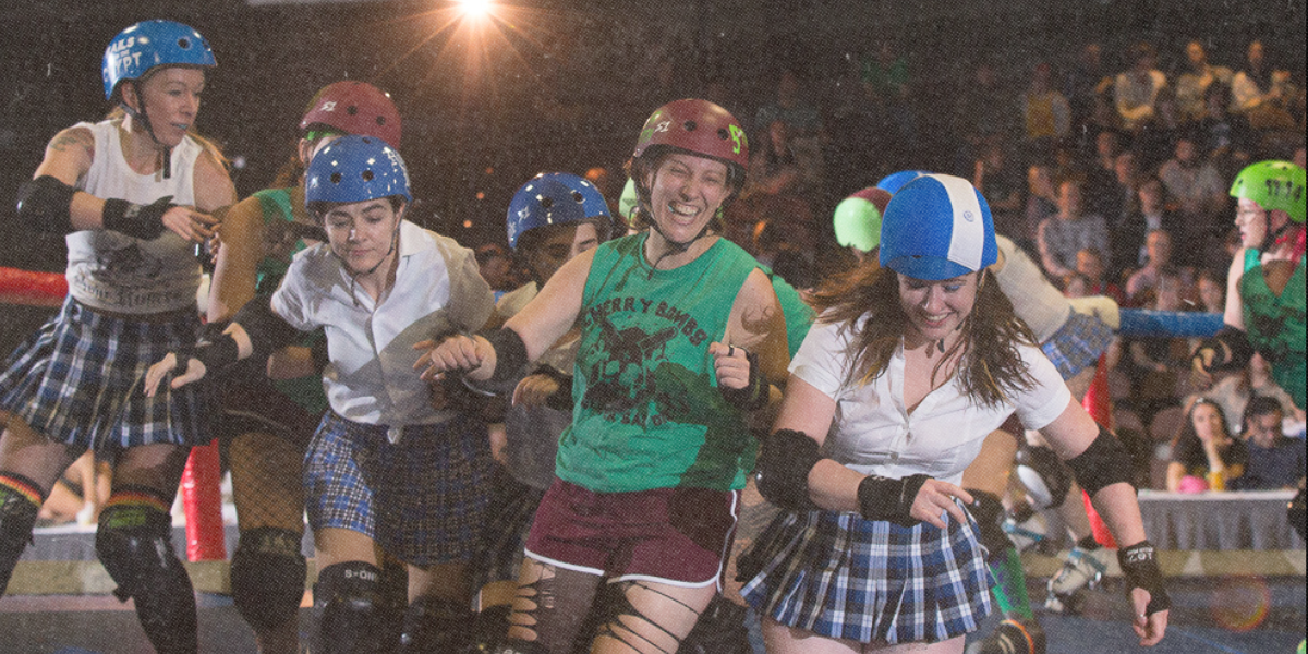 A group of queer smile as they bump into each other on a roller derby rink.