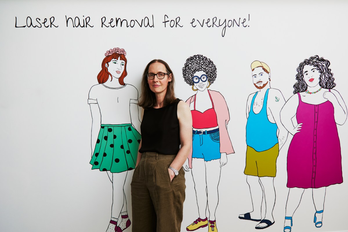 Djuna Day poses in front of a mural that says Hair removal for everyone