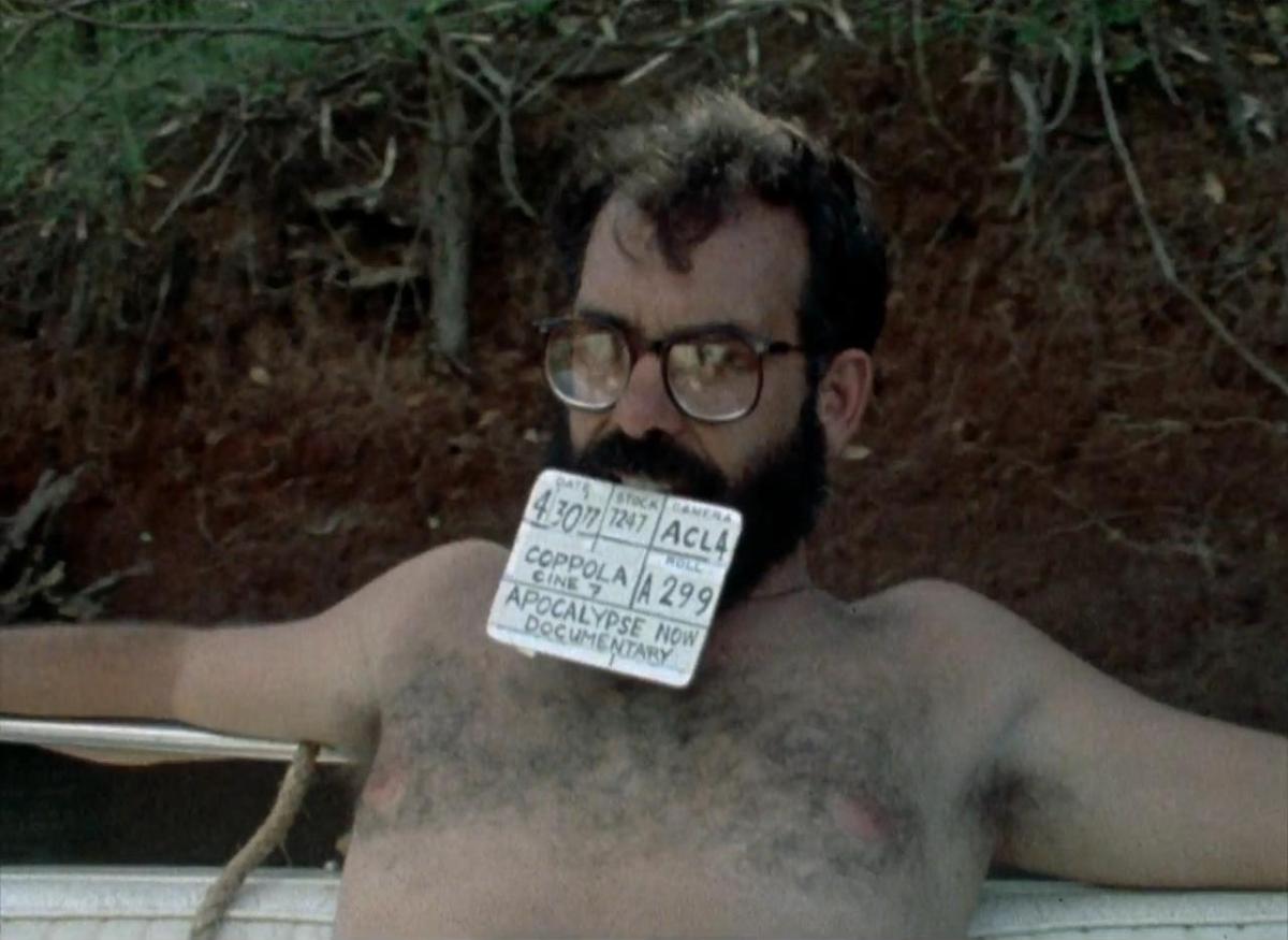 Francis Ford Coppola shirtless holds a clapboard in his teeth