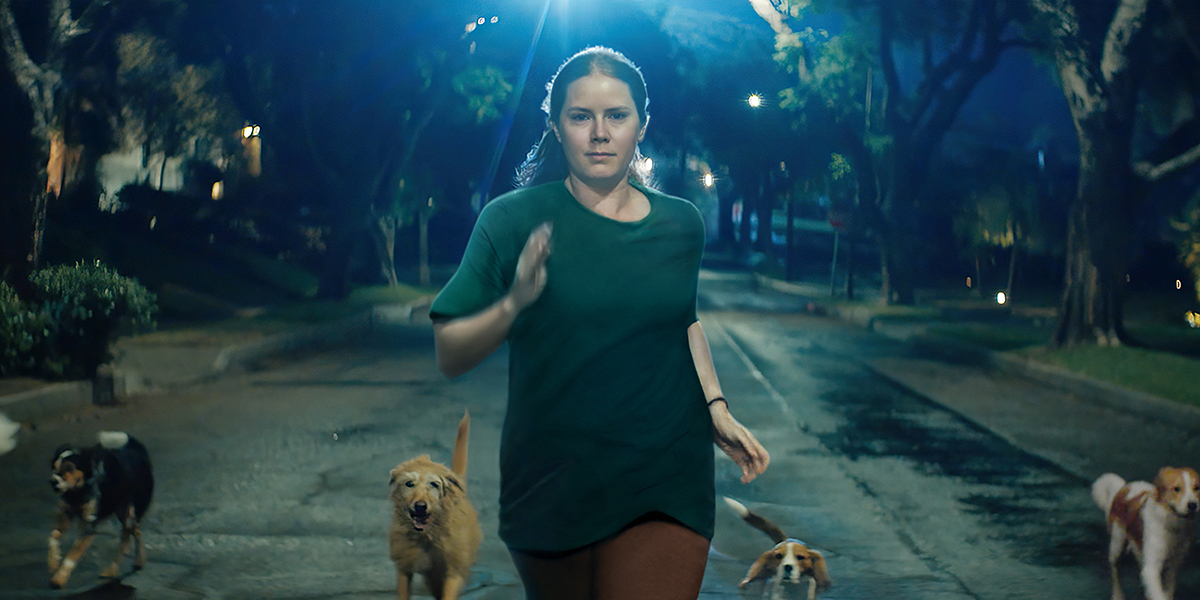 Amy Adams runs at night with dogs following behind her in Nightbitch.