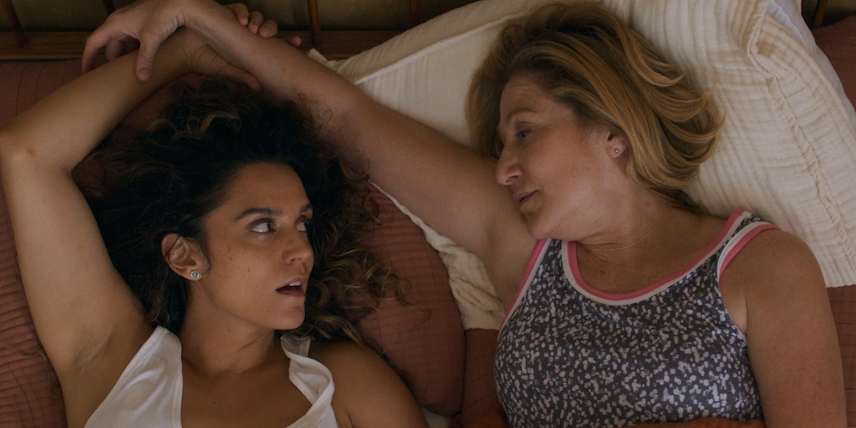 Edie Falco and Sepideh Moafi lie in bed together in I'll Be Right There.