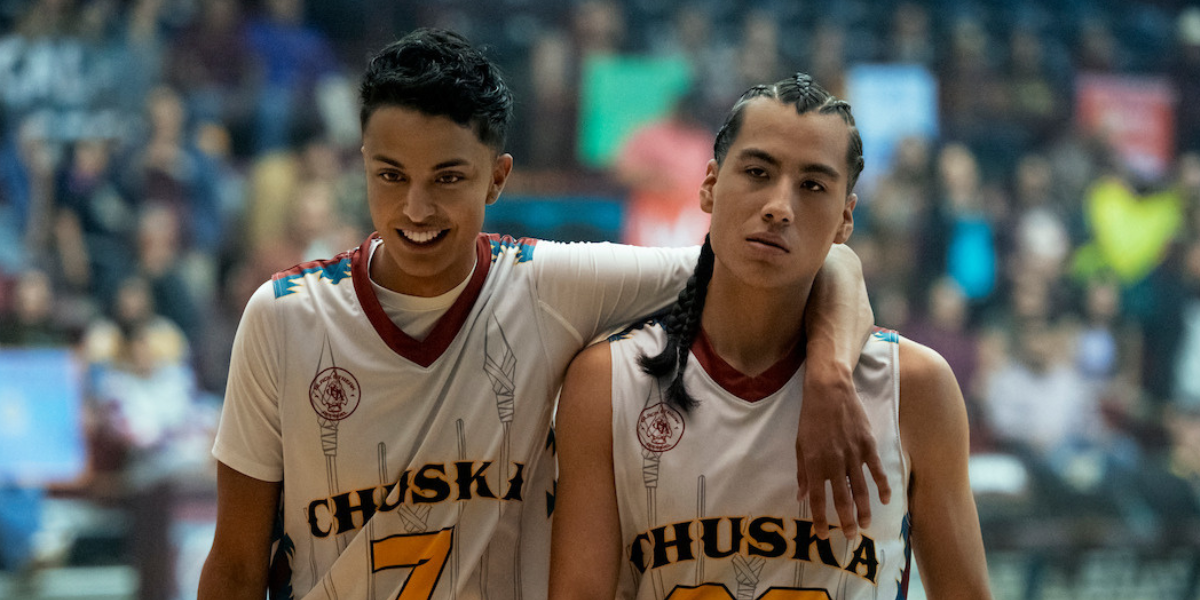 Two Indigenous teen boys in basketball jerseys pose with an arm around each other in Rez Ball.