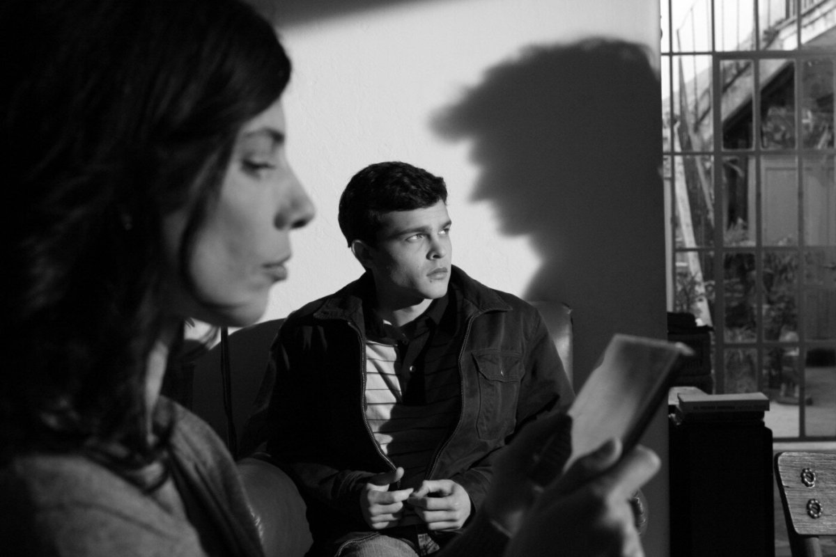 A black and white image of Maribel Verdú's profile with Alden Ehrenreich sitting behind her.