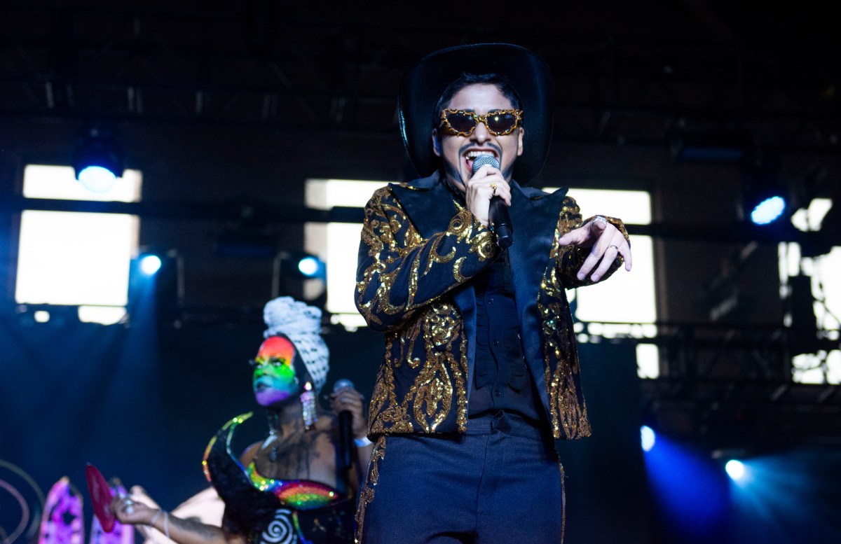 Bobby Pudrido performs on stage in sunglasses and a gold and black jacket.