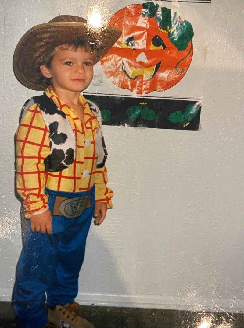 Drew, age 5, dressed as Woody from Toy Story poses next to a jack-o-lantern picture