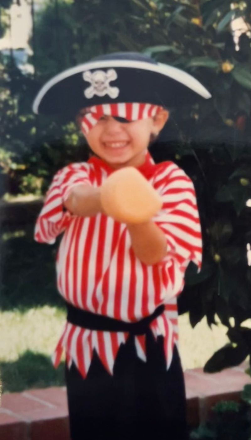 Drew, age 6, wears a pirate costume and thrusts forward some sort of plastic weapon.