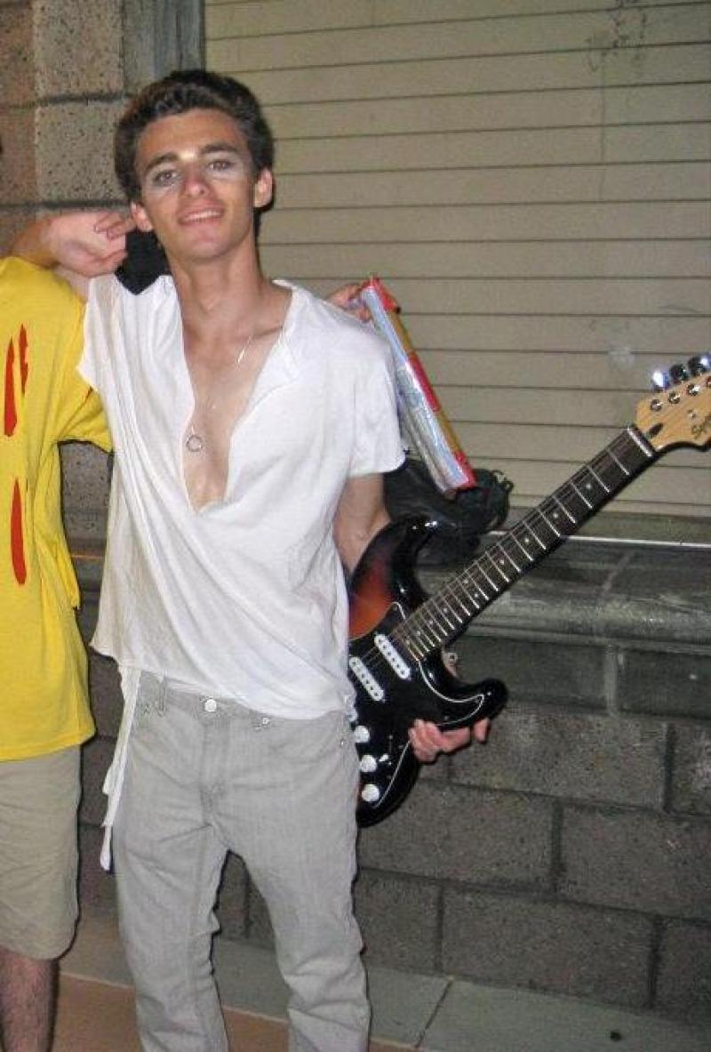 Drew, age 17, in a white torn t-shirt and lightwash pants, glam make up, and a guitar.