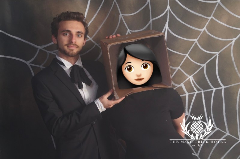 Drew, age 22, dressed in a suit with a goatee holding a box attached to a girl to make her head look like it's in the box. An emoji covers the girl's face.