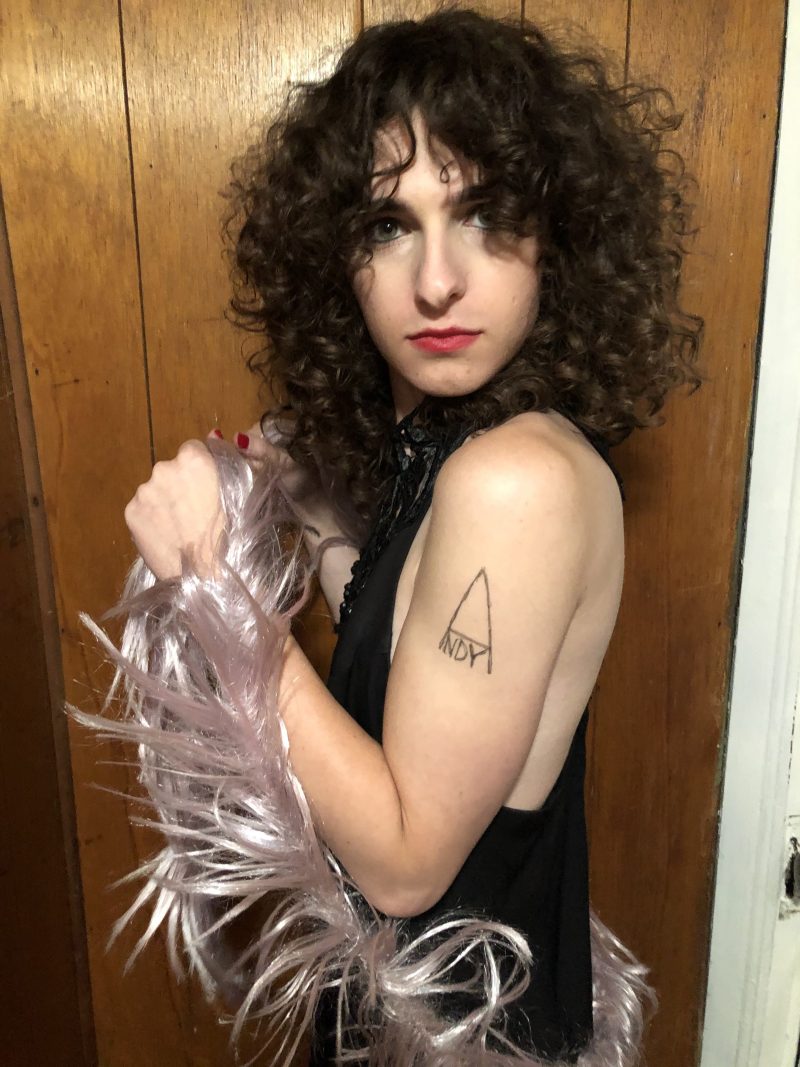 Drew in a black dress with a pink feather boa has a fake Andy tattoo on her arm.