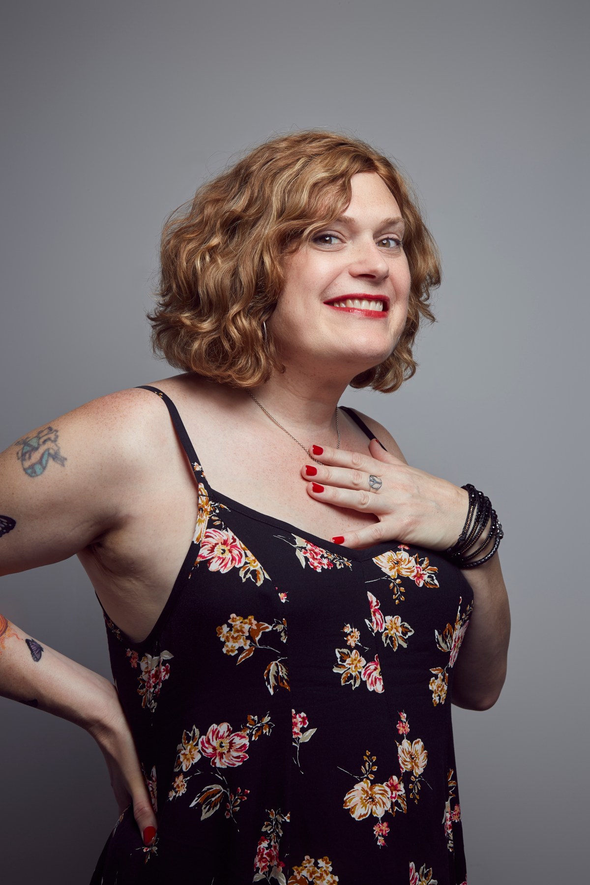 Lilly Wachowski interview: Lilly poses with one arm on her back and another on her chest smiling at the camera in a black dress with a flower print.